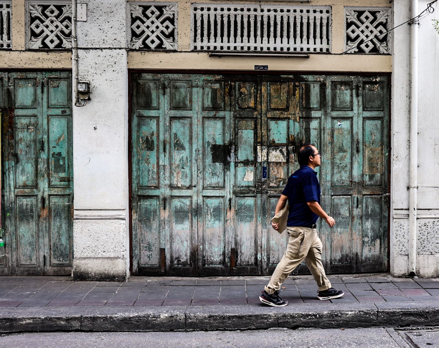 Man wearing face mask walking past weathered turquoise wooden doors on a vintage urban street.