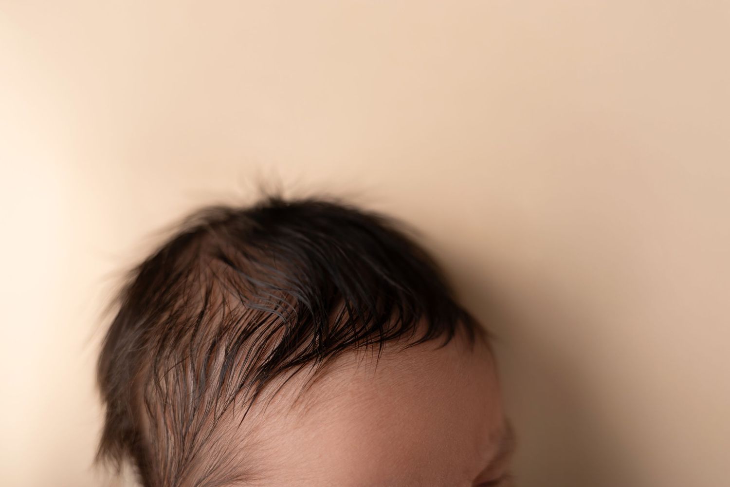 A backlit partial head shot showing dark hair silhouetted against a beige background.