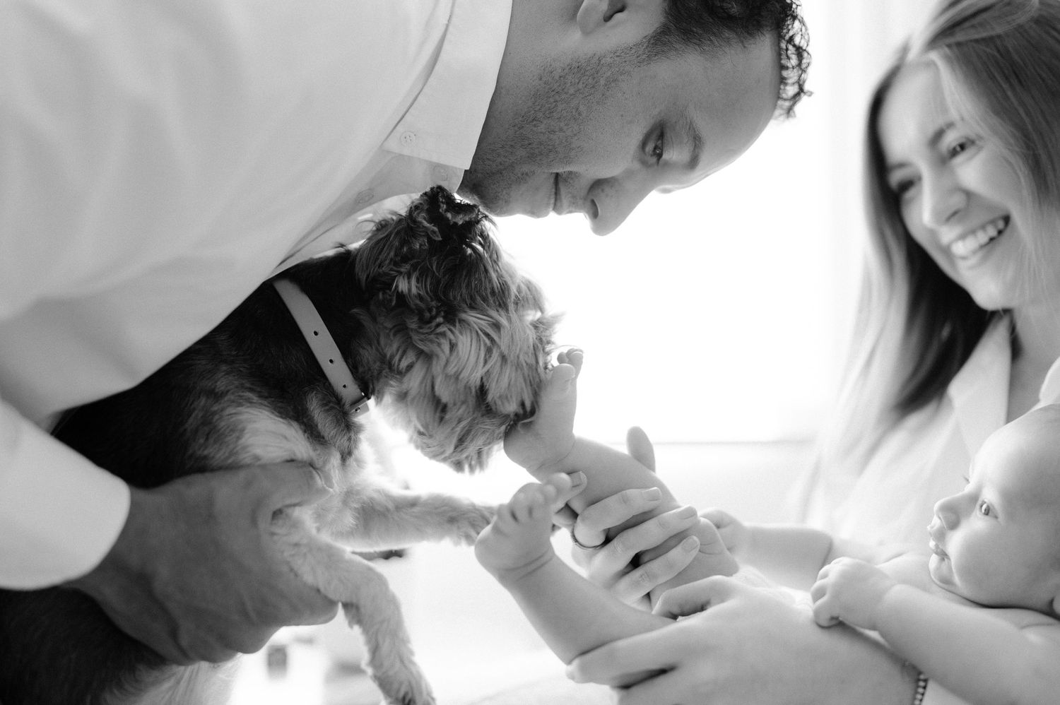 Black and white photo of family sharing joyful moment with baby.