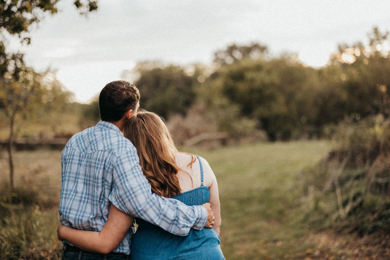 Couple embracing while sitting outdoors at sunset with trees in background.