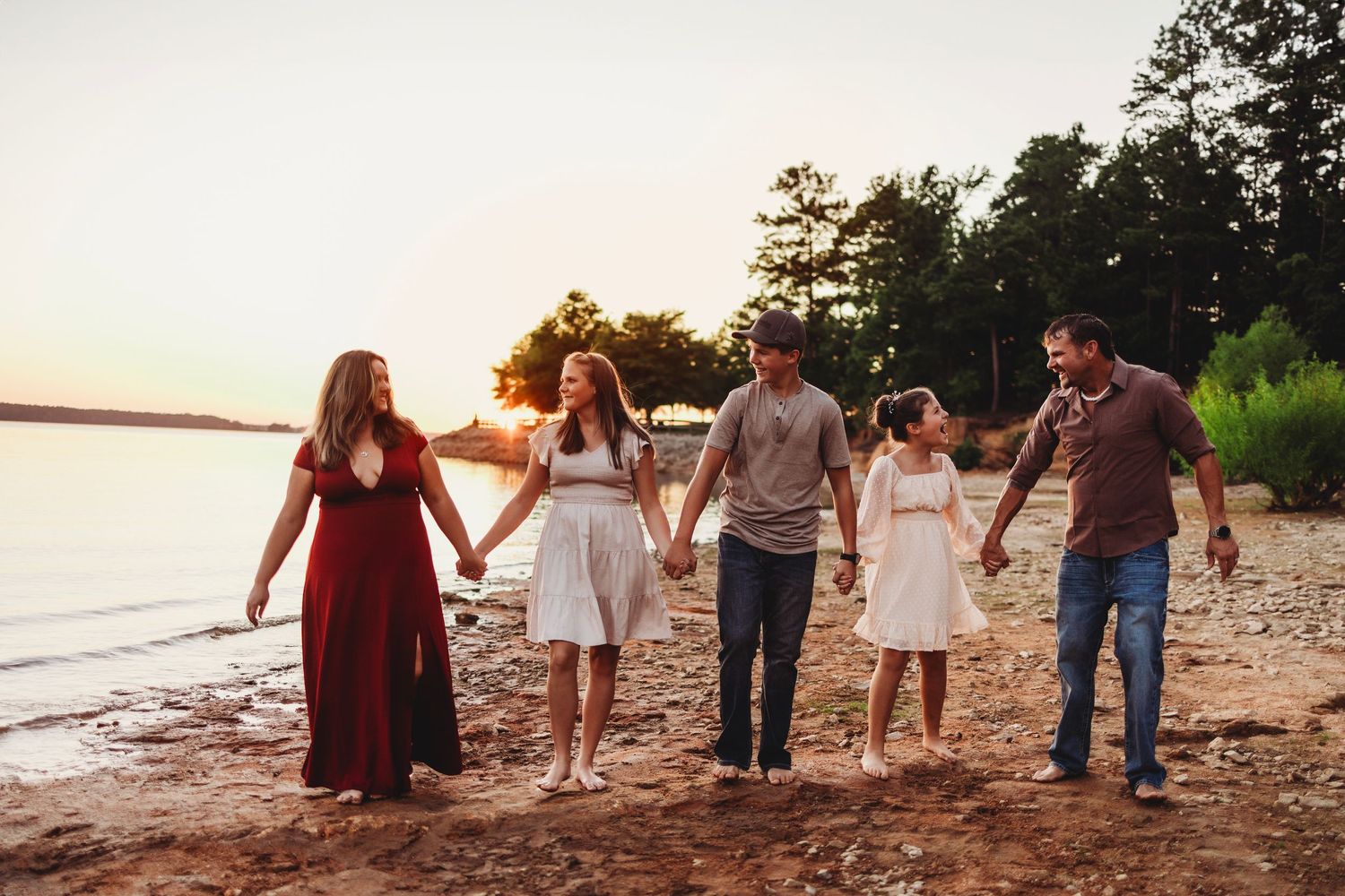Group of people walking hand in hand along a beach shoreline at sunset.