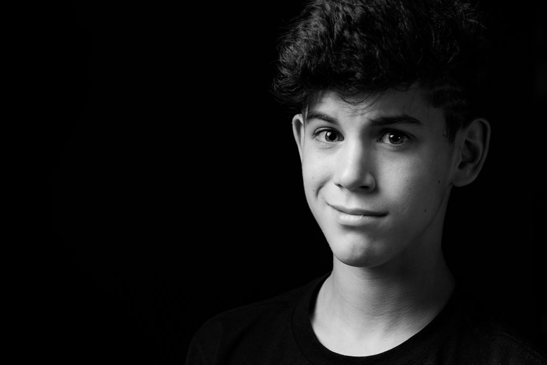 Black and white portrait showing a young person with dark curly hair against a dark background.