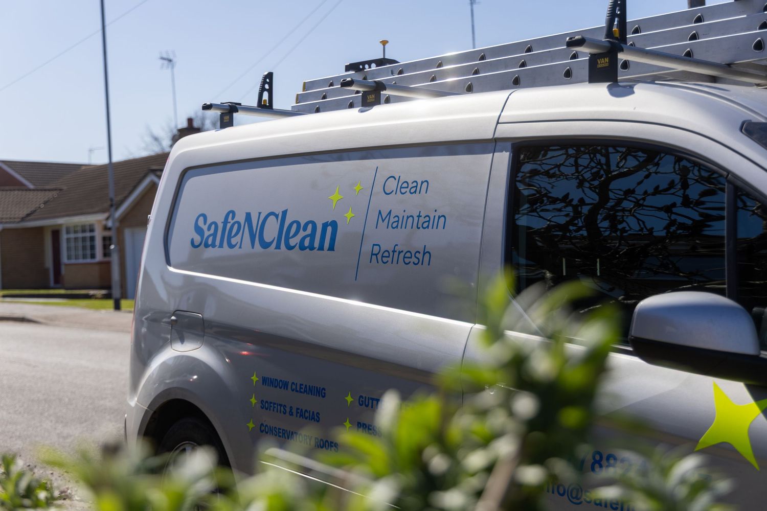 A white Safe & Clean service van with company branding and roof racks parked outside a residential building.
