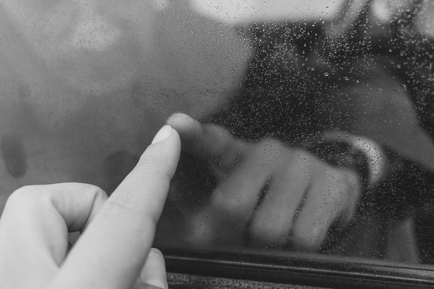 Black and white close-up of a finger touching a reflective glass surface.