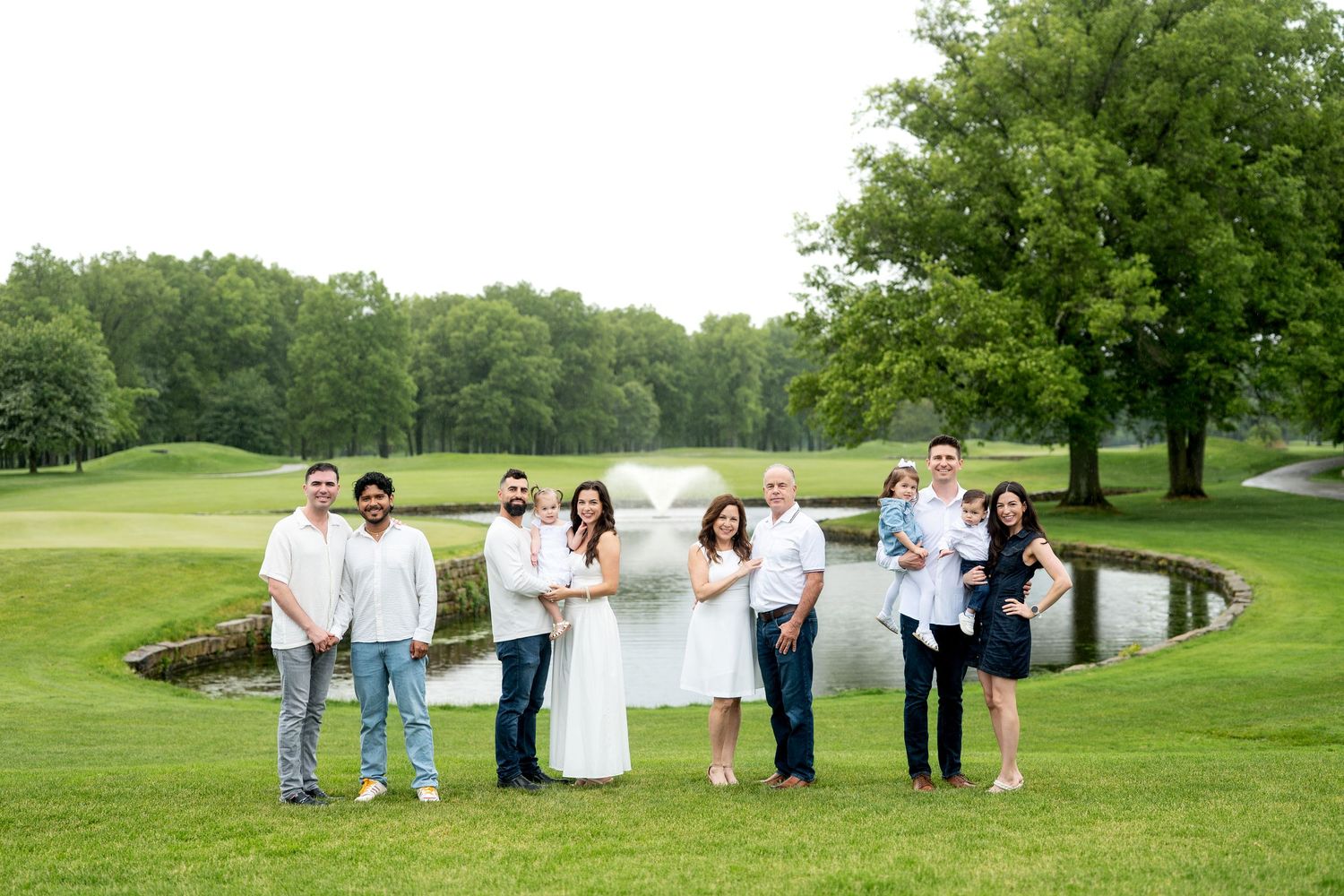 Couples posing romantically on lush green golf course lawn near scenic pond and trees at outdoor wedding celebration.
