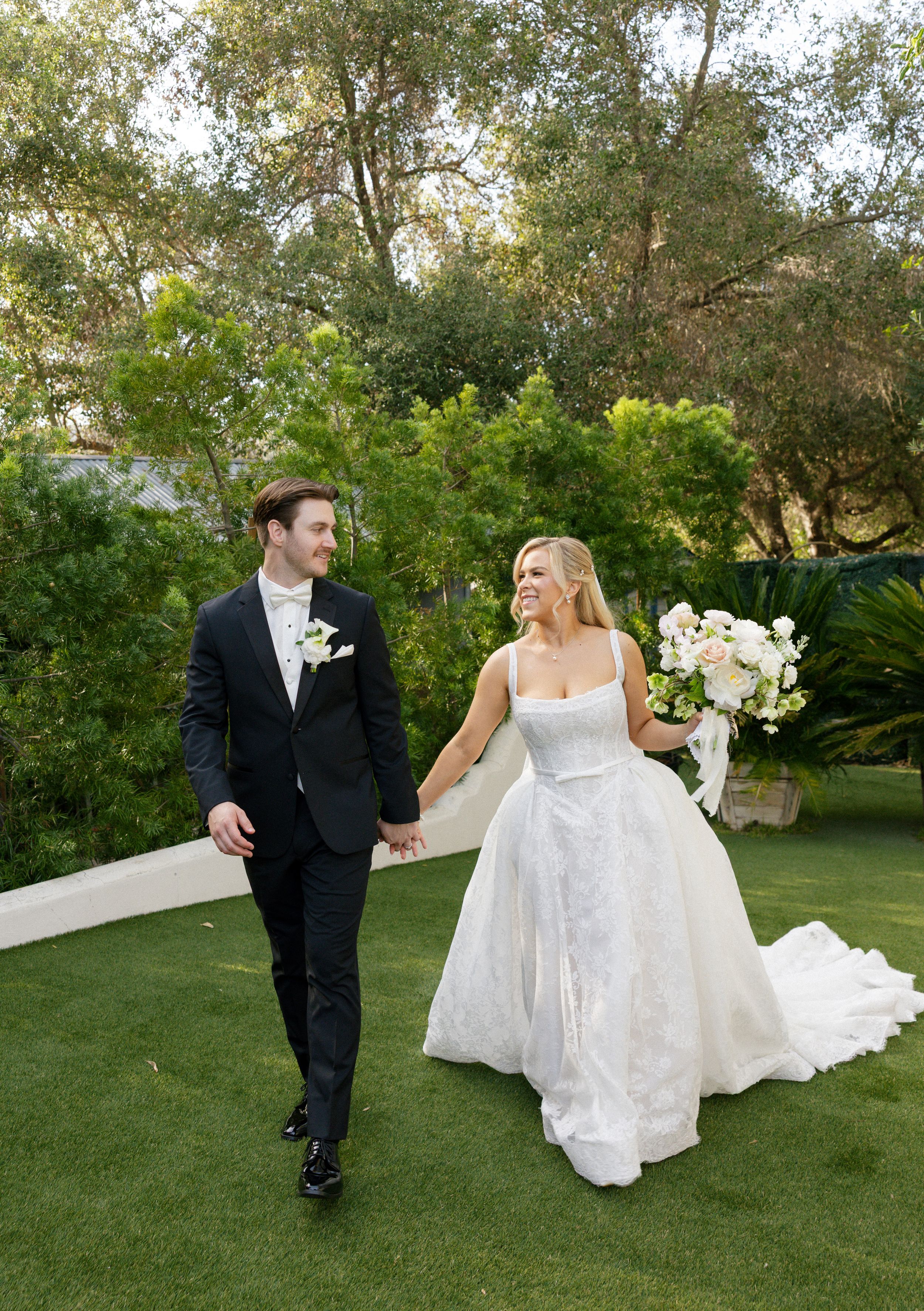 Bride and groom share first kiss at outdoor wedding ceremony under oak trees with seated guests.