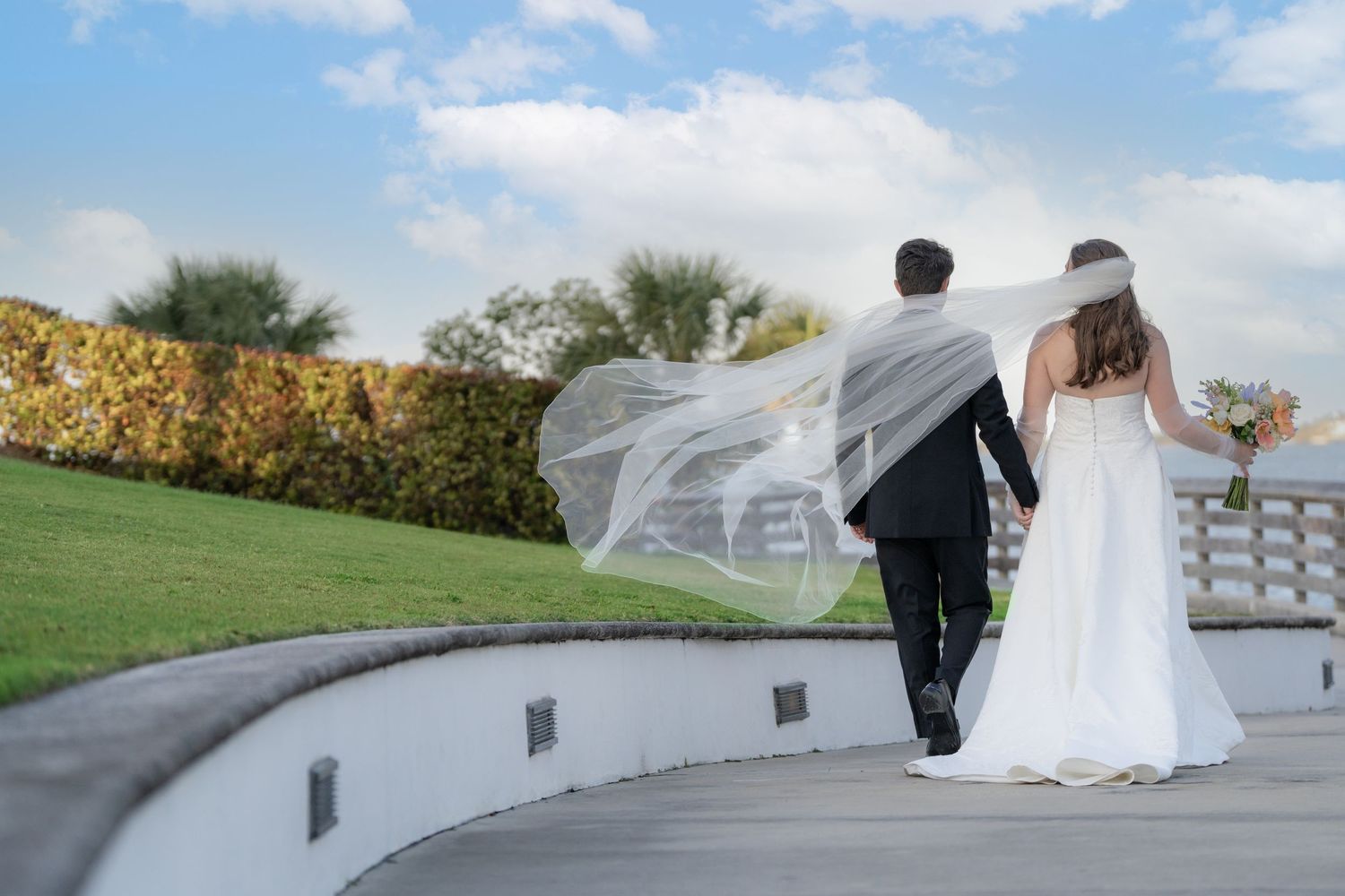 Wedding party walks on green lawn before white mansion, groomsmen in gray suits, bridesmaids in yellow dresses.