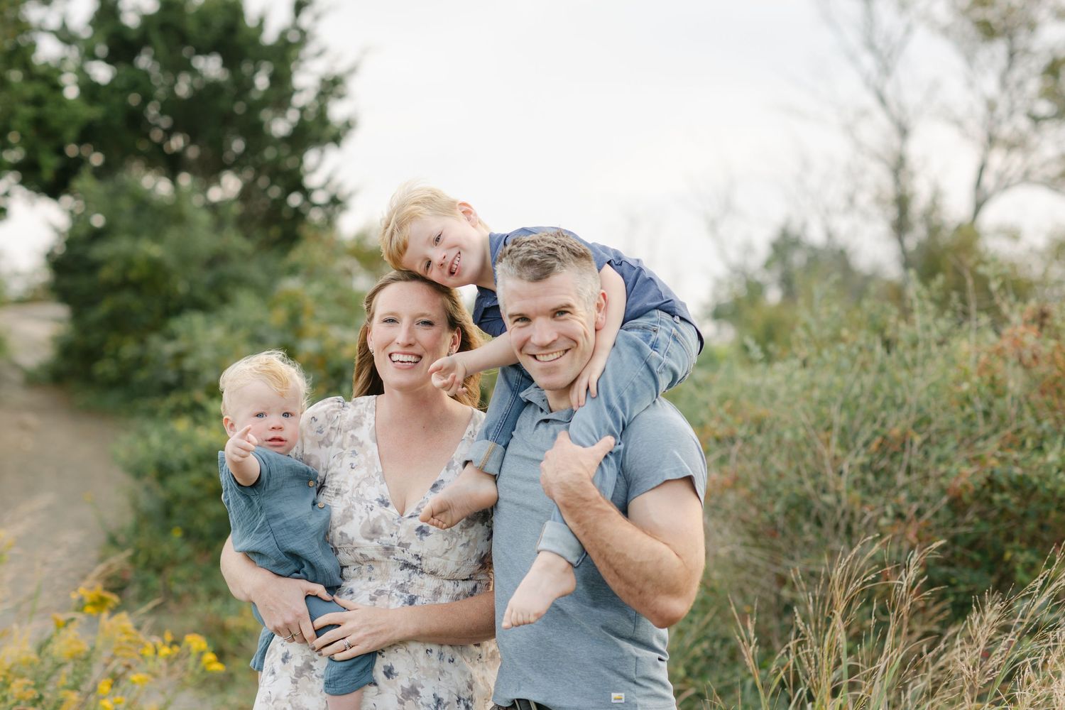 A family shares joyful moments together during an outdoor photo session in a natural setting with tall grass and greenery.