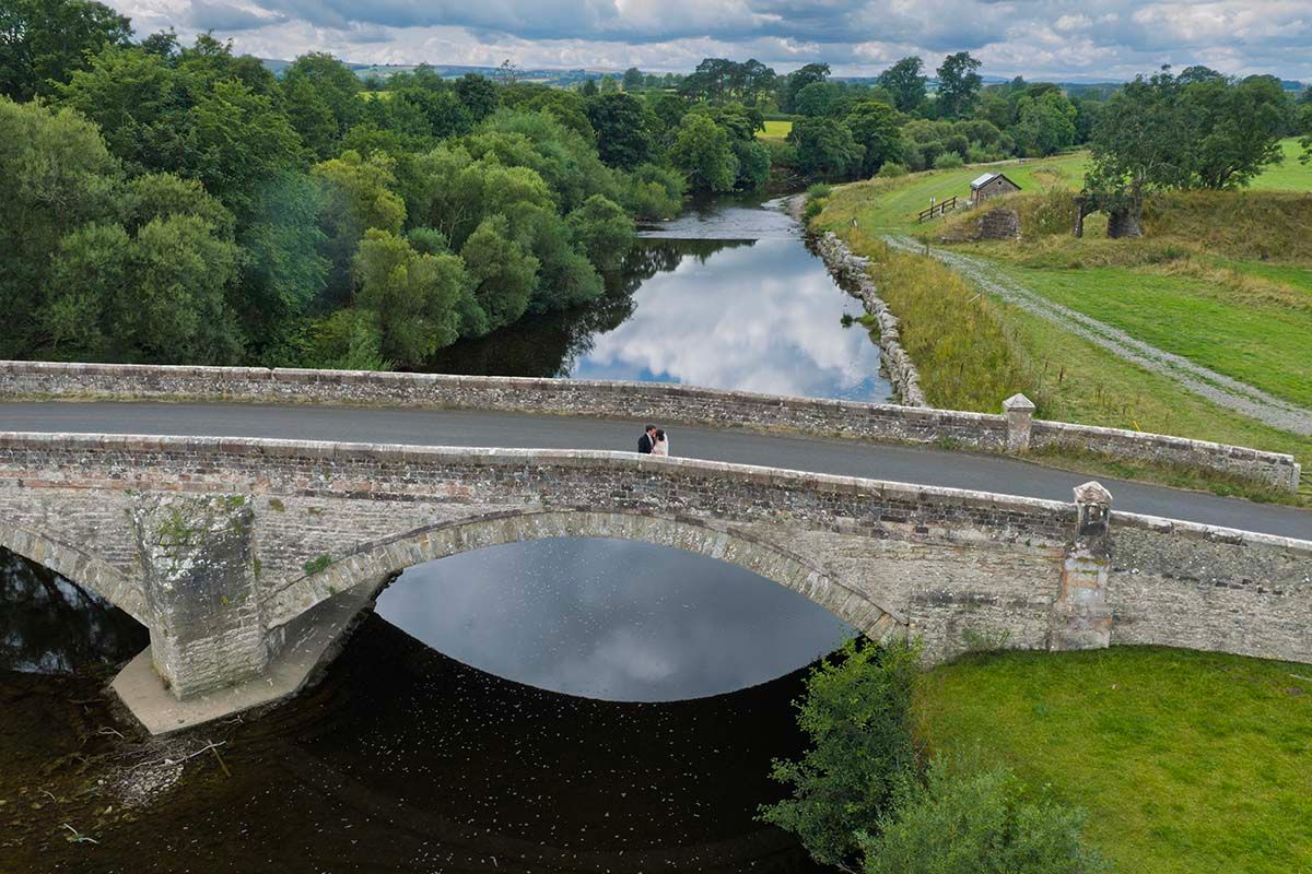 Historic stone arch bridge spanning a calm river in lush green Irish countryside landscape.