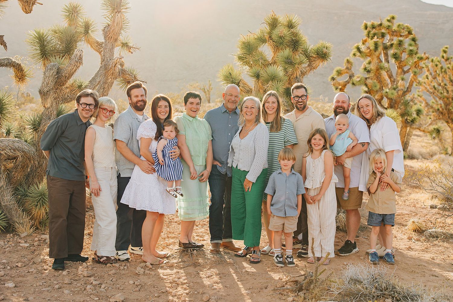 Large family group portrait outdoors in Joshua Tree desert landscape, smiling together in casual attire at golden hour.