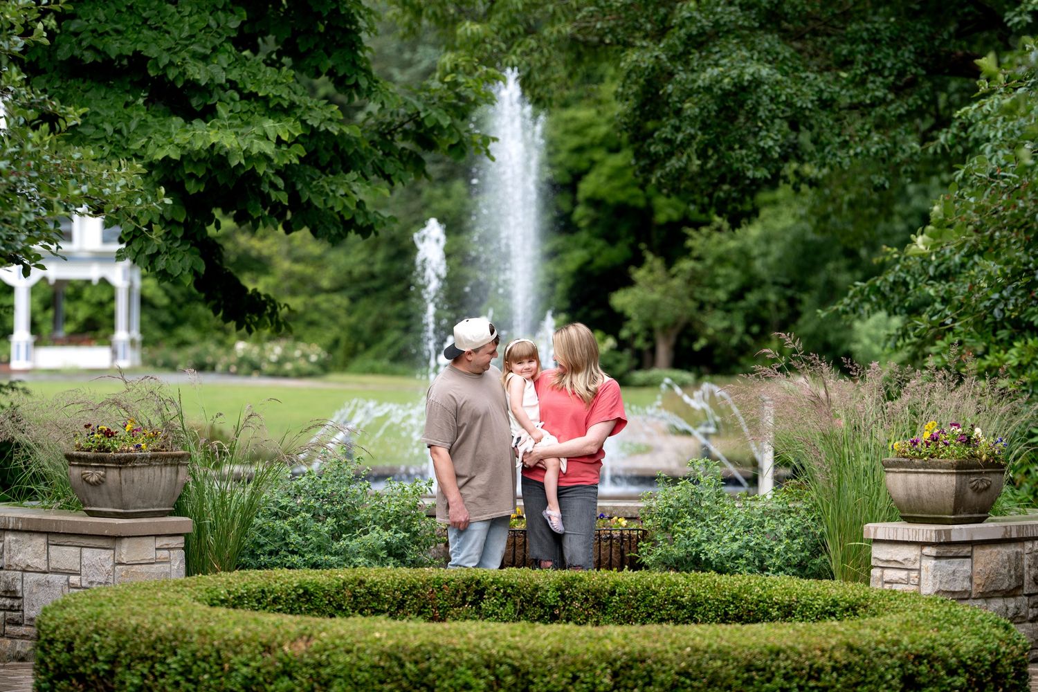 Family enjoying a lush garden with a fountain and green hedges on a sunny day.