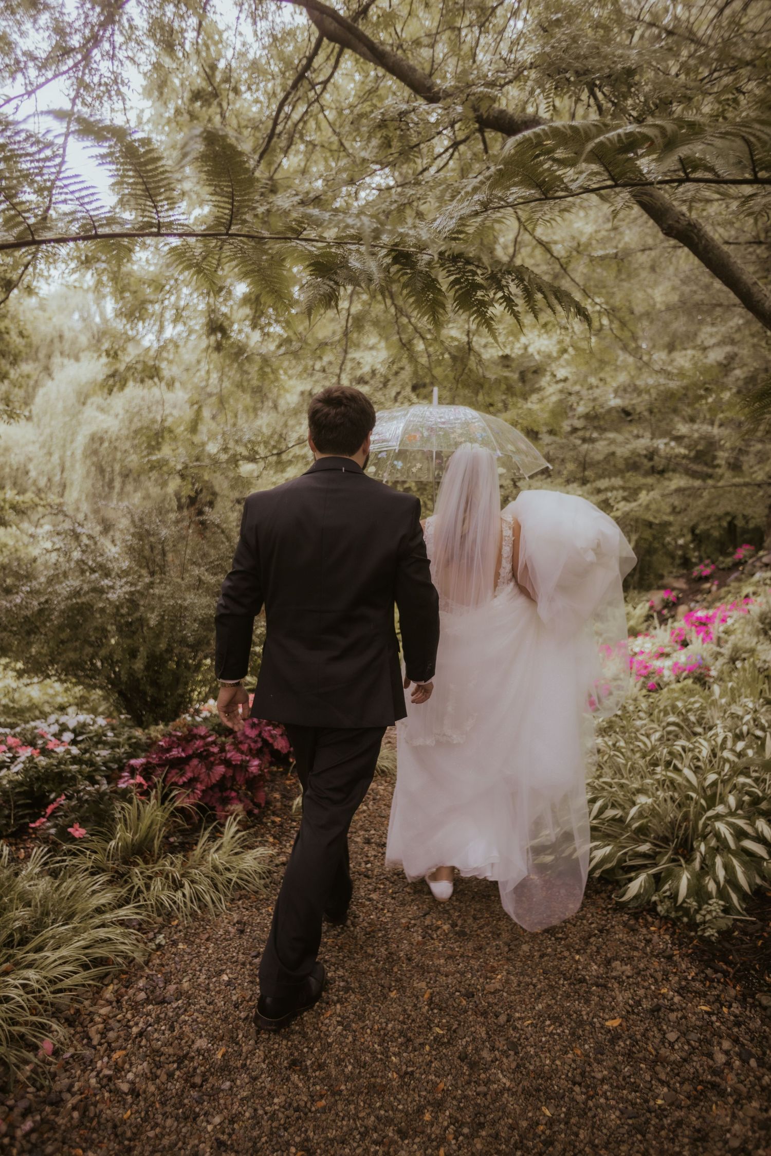 Bride and groom walking hand in hand through a lush garden path on their wedding day at Everlastings in the Wildwood in Owosso Michigan.