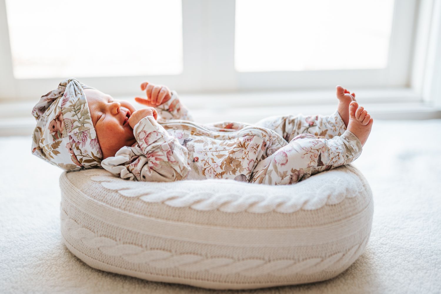Newborn baby sleeping peacefully in a white knit lounger pillow wearing a floral outfit taken by an in-home Melbourne newborn photographer.