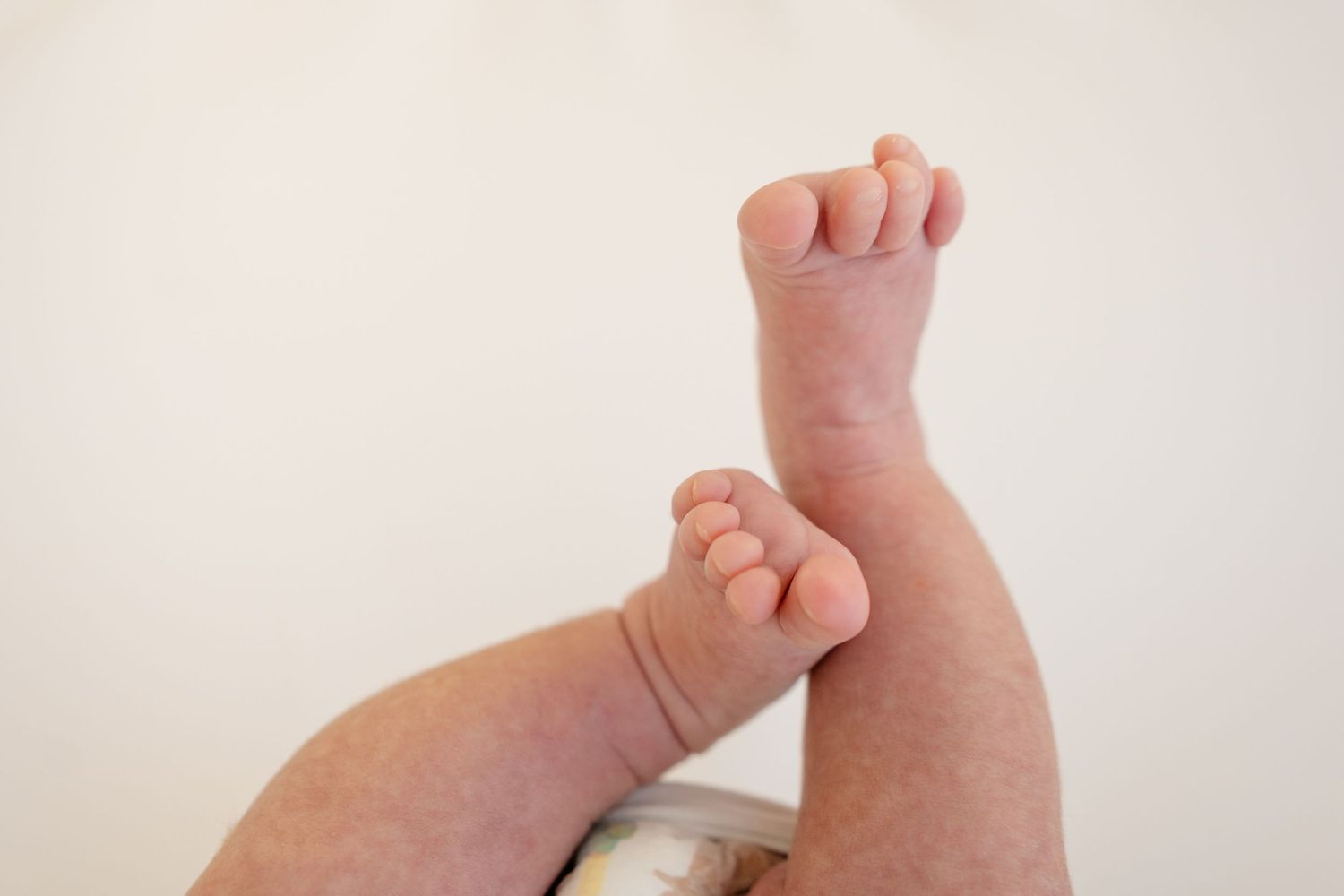 Close-up of adorable baby feet and chubby legs raised in the air against a white background.