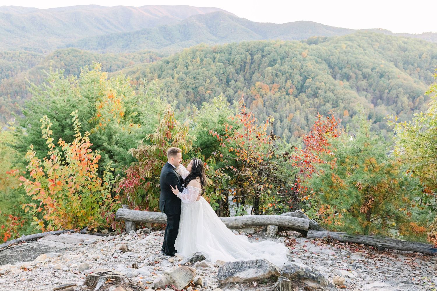 Bride and groom share a romantic kiss on a rocky overlook surrounded by colorful autumn mountain foliage.