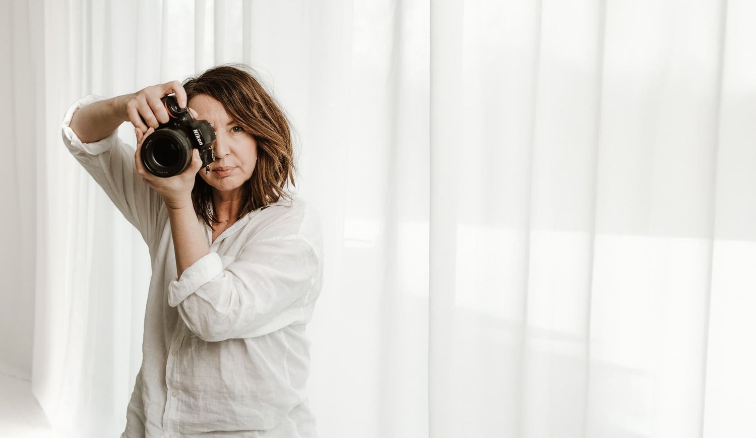 Fotograf Veronica Eng i sin vita studio i Jönköping Mullsjö, håller i sin systemkamera., som är en Nikon.
