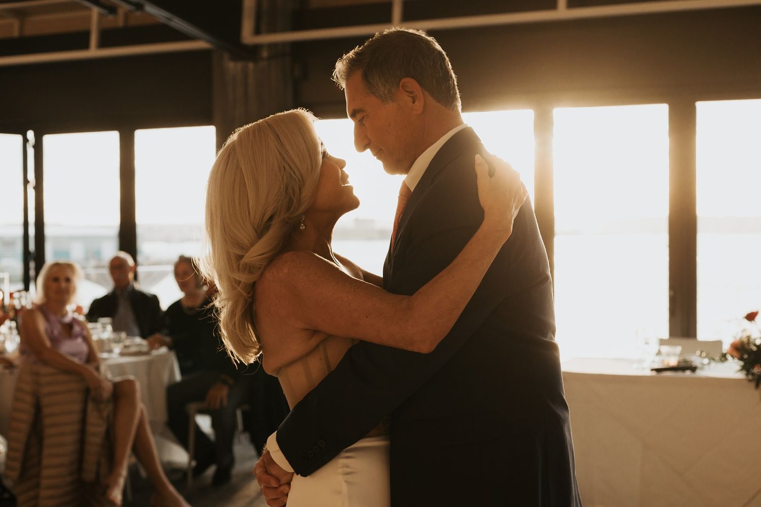 Silhouettes of a bride and groom dancing at sunset during a wedding celebration.