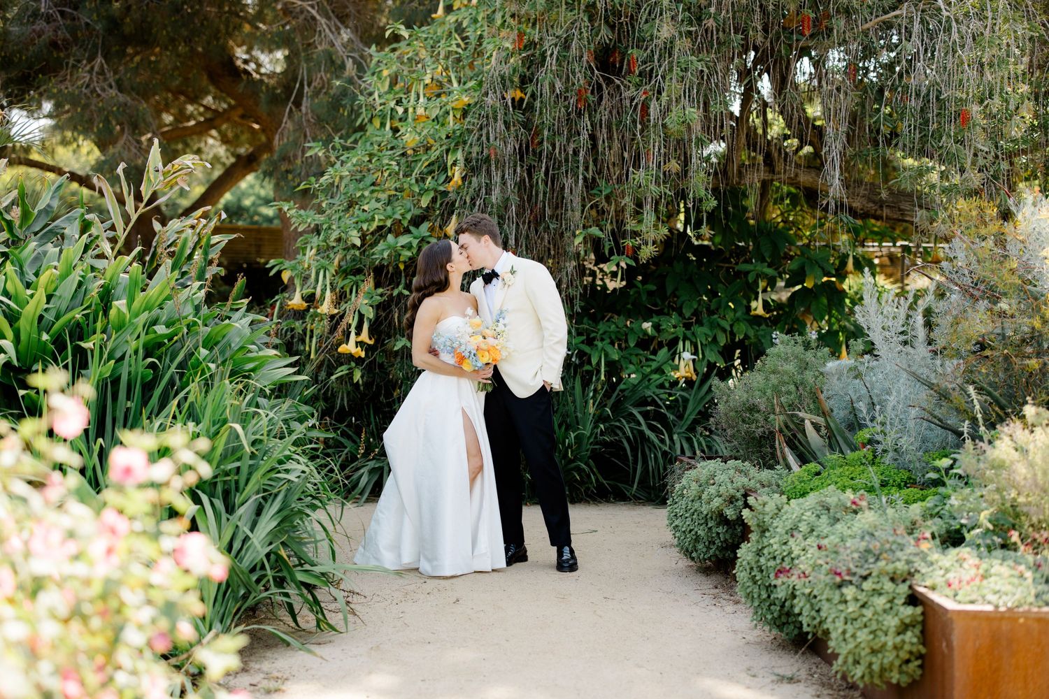 Garden pathway lined with lush greenery and flowers creates a romantic wedding setting.