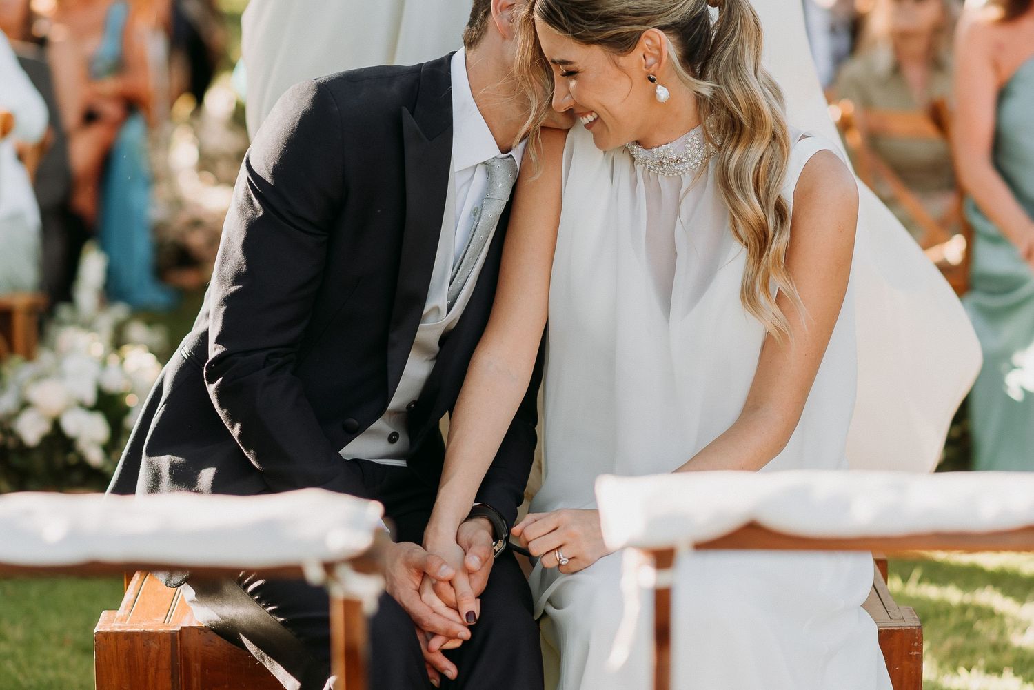 Couple sharing an intimate moment at outdoor wedding ceremony, holding hands and smiling together in elegant attire.