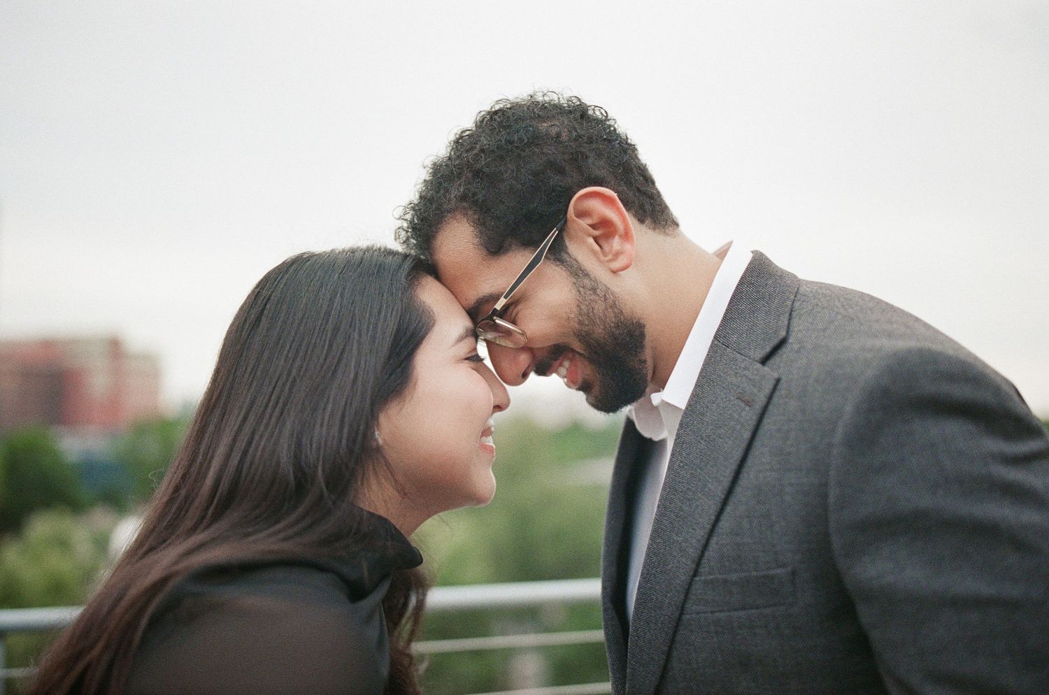 A couple shares an intimate moment, touching foreheads and smiling, outdoors on a balcony.