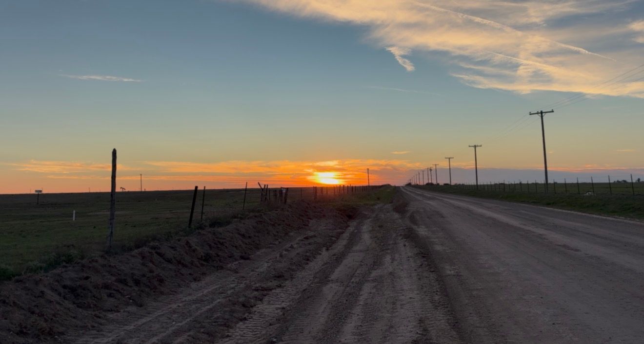 Stunning rural sunset over a dirt road with utility poles, green fields, and vibrant orange sky in a peaceful countryside.