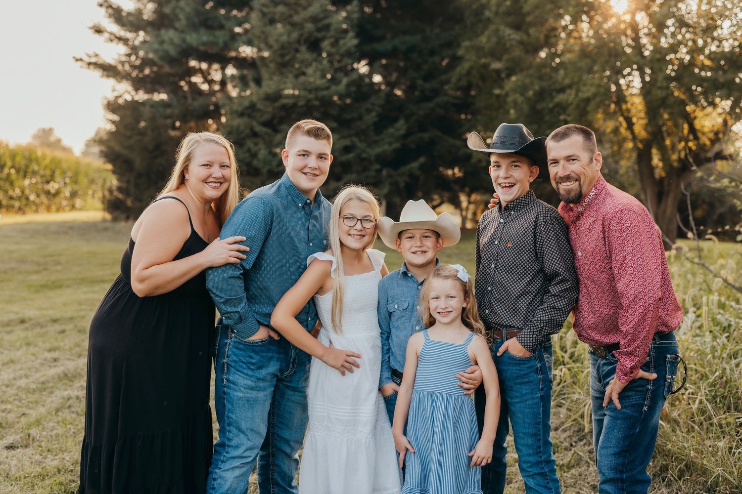 A joyful family of seven poses together outdoors in golden hour light, wearing coordinated blue and denim outfits.