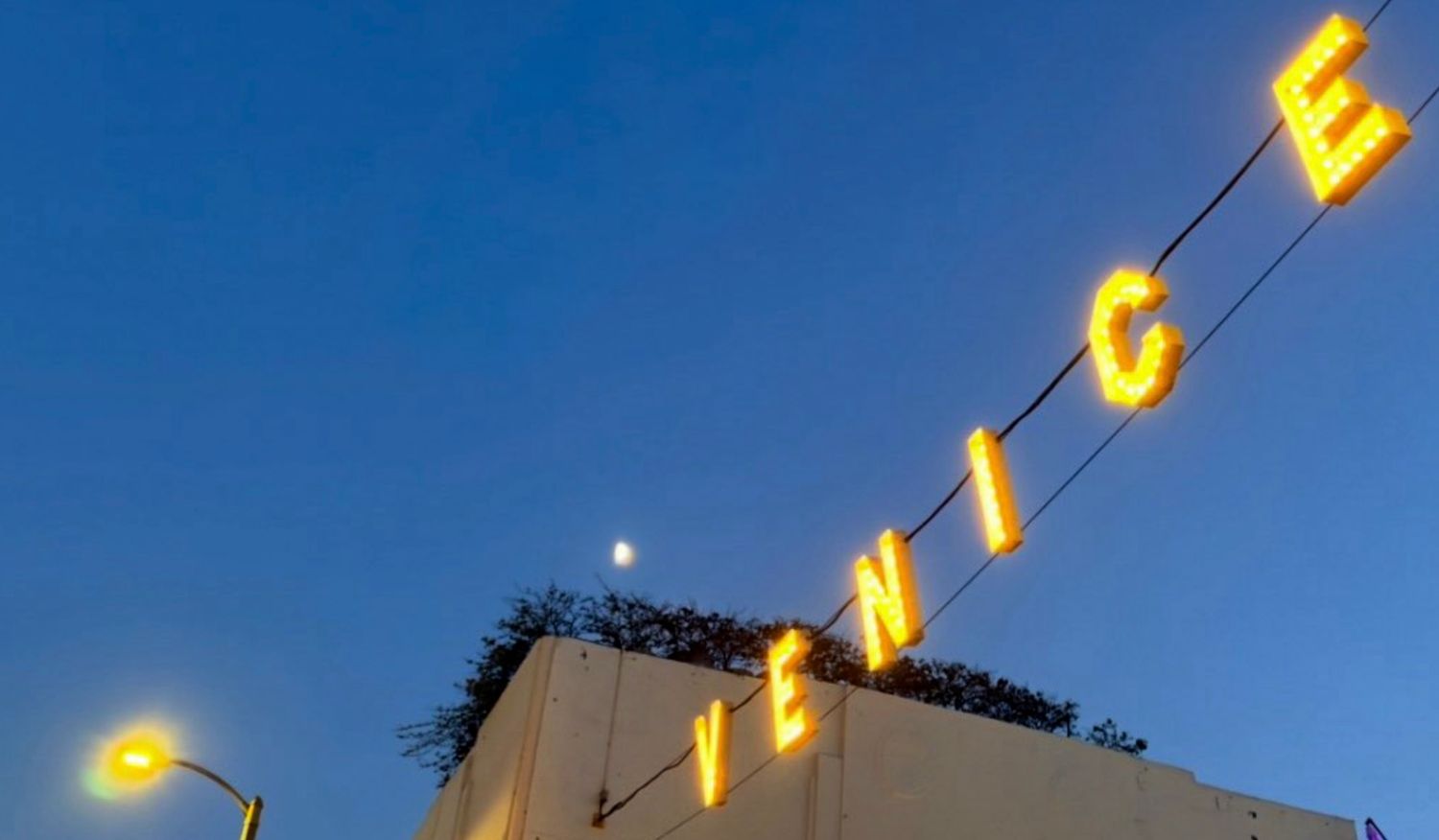 Illuminated yellow VENICE sign glowing against a twilight blue sky with a crescent moon visible.