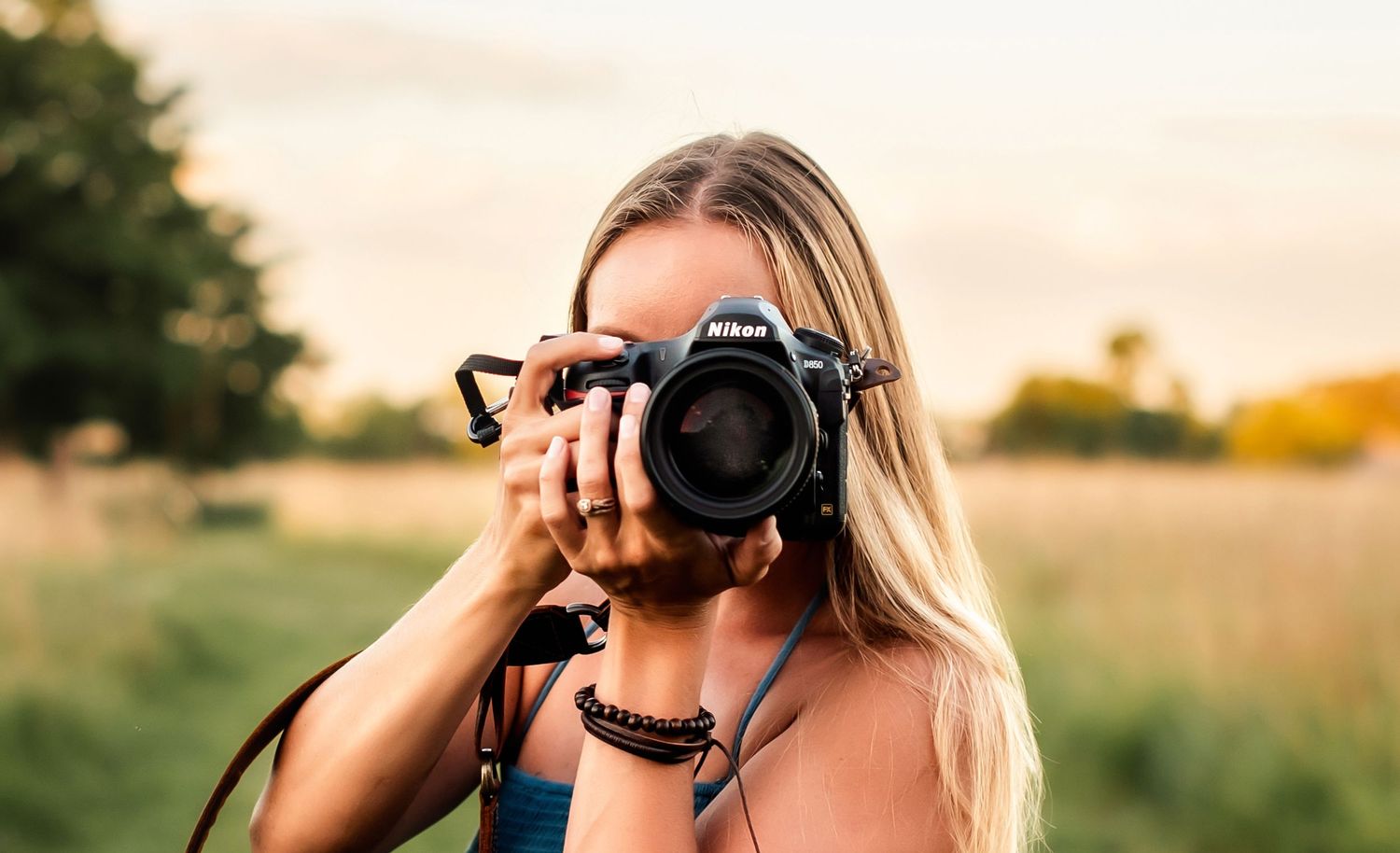 Photographer holding professional DSLR camera in golden field during sunset with bokeh background.