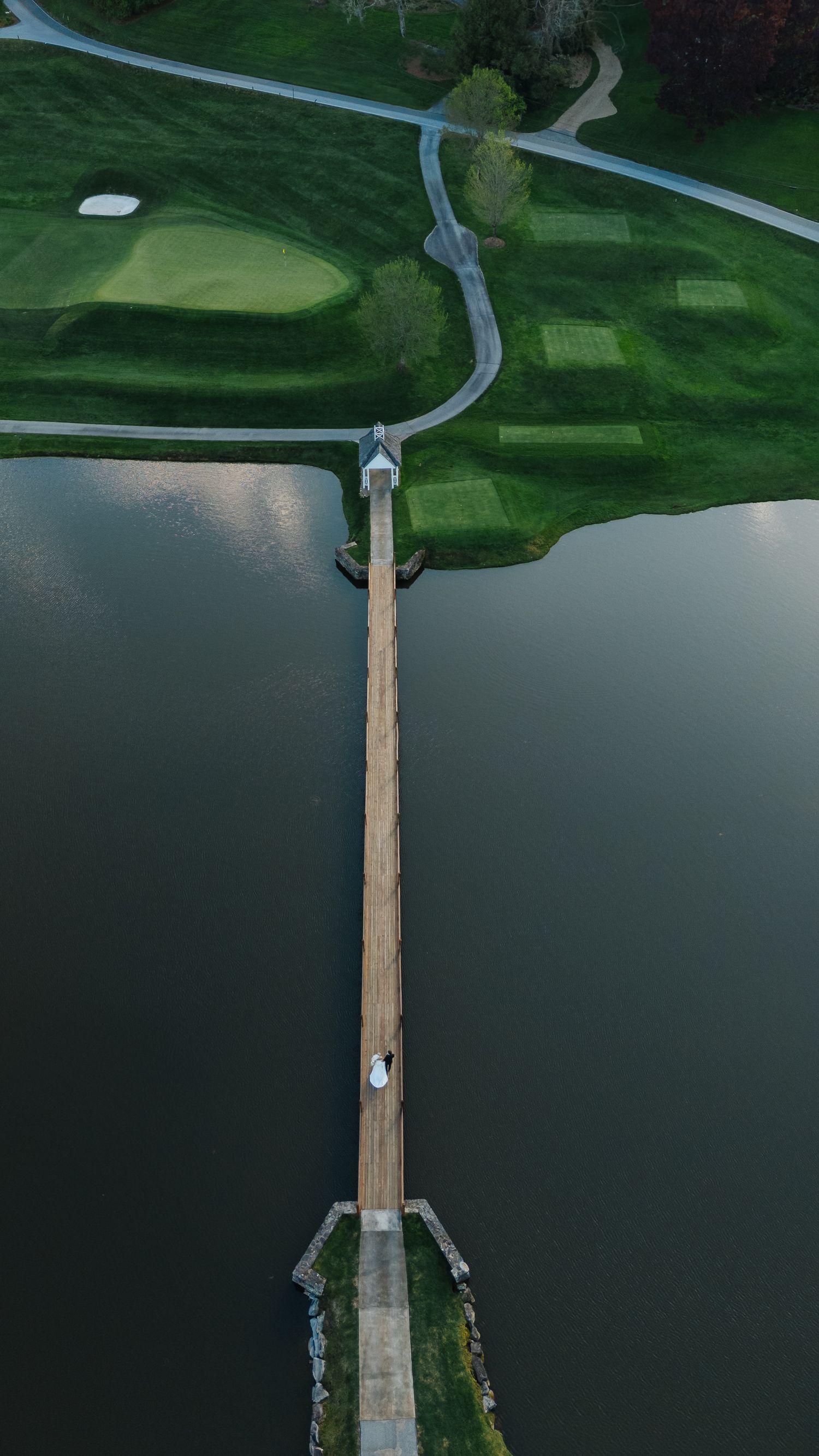 Aerial view of a wooden pier extending into dark waters surrounded by green golf course.