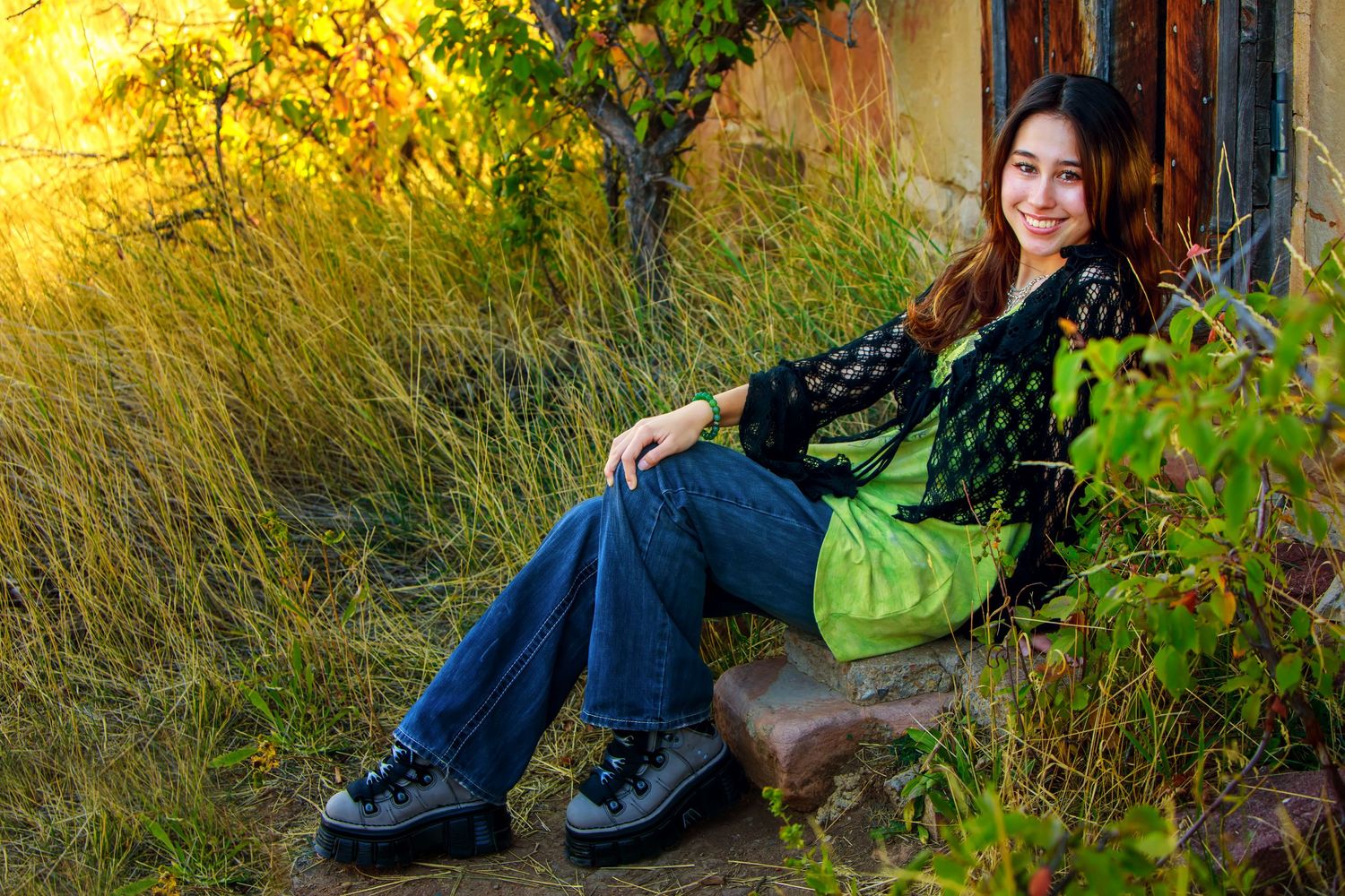 Person sitting outdoors on tree trunk with autumn foliage during golden hour in casual clothing.