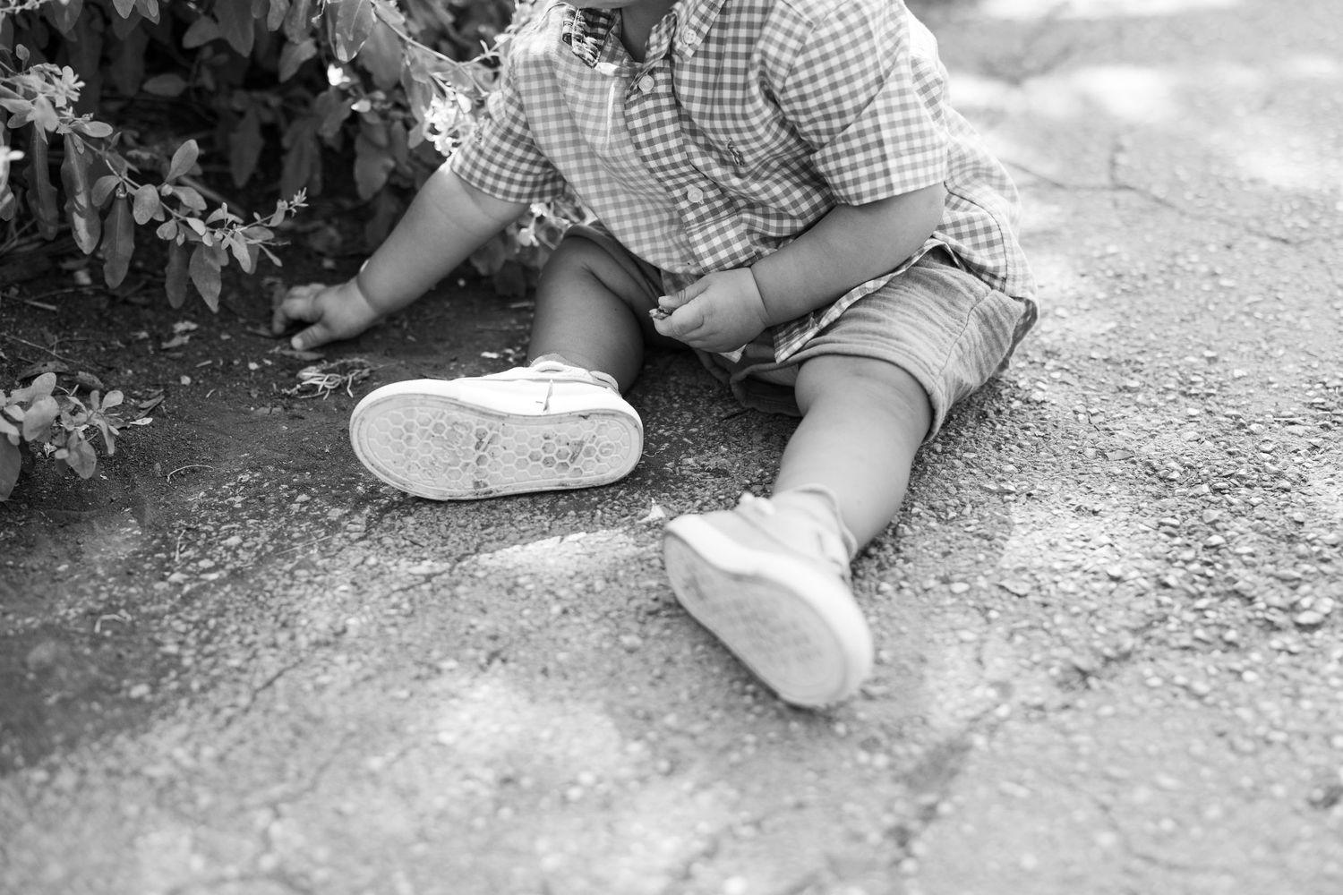 A black and white close-up of someone's feet and legs sitting on the ground.