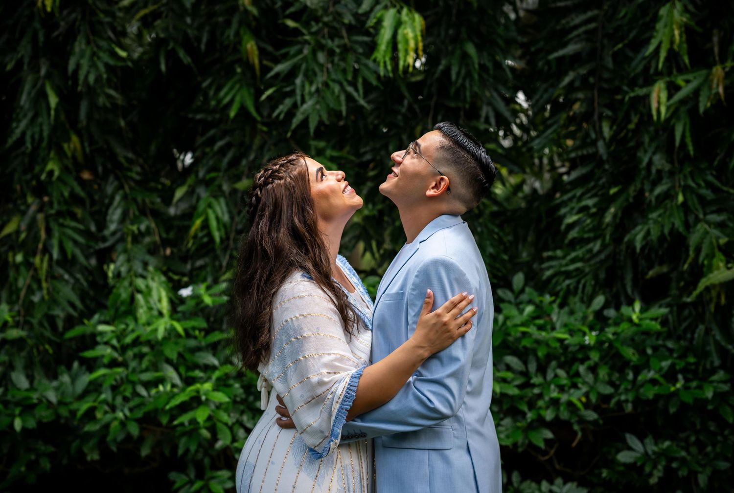 A joyful engagement photo shows a couple laughing together against lush tropical greenery.