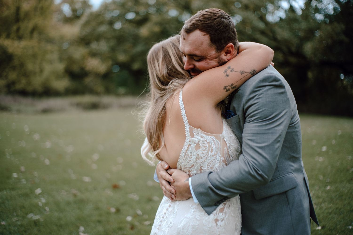 A tender embrace between newlyweds in formal attire on a grassy field.