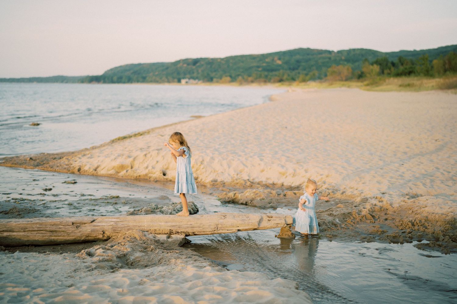 Two children explore a driftwood log on beach at sunset.