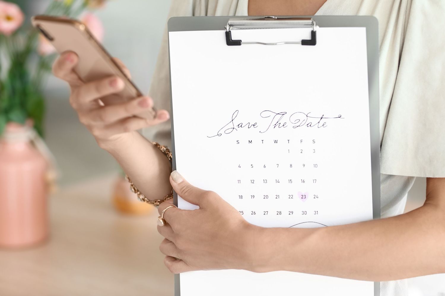 Someone holding a calendar with pink text on a minimalist white design in a soft daylight setting.