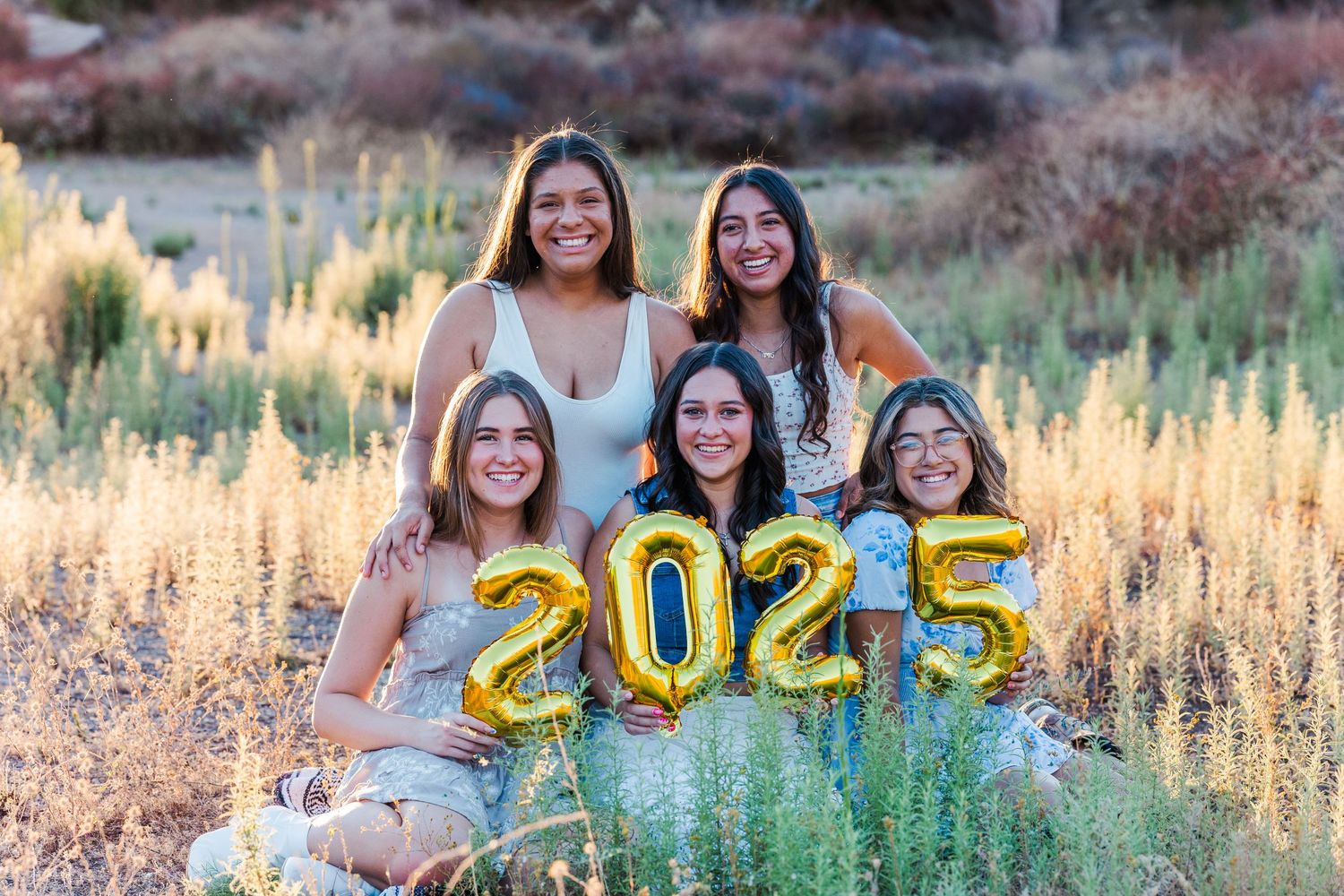Group photo with gold 2025 balloons in a scenic outdoor setting at sunset.