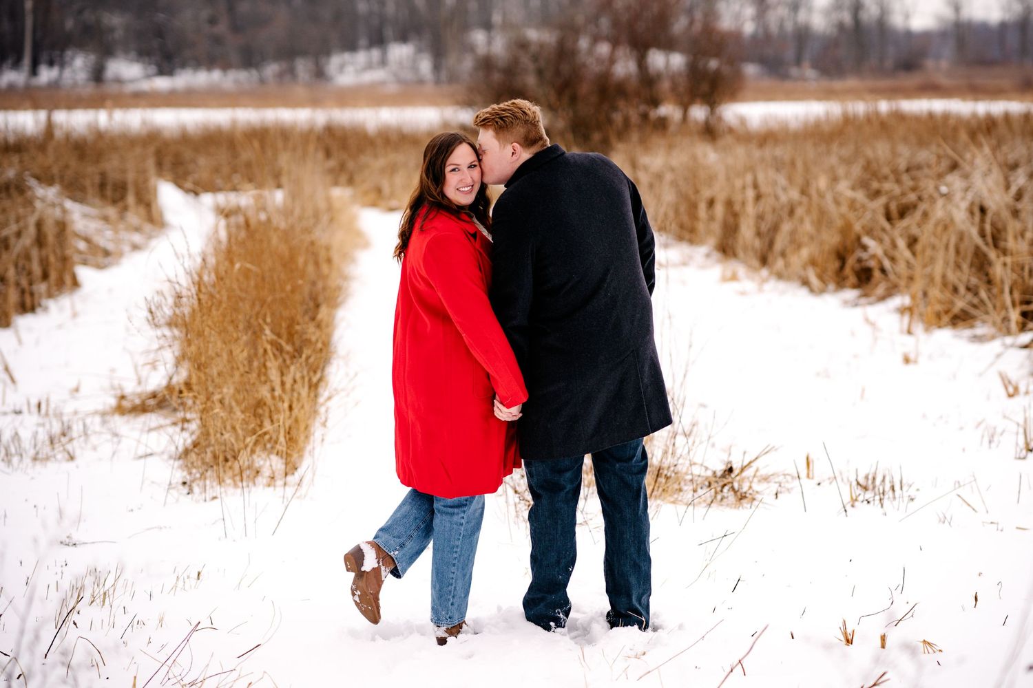 A tender winter moment between two people in a path through golden grass and snow.