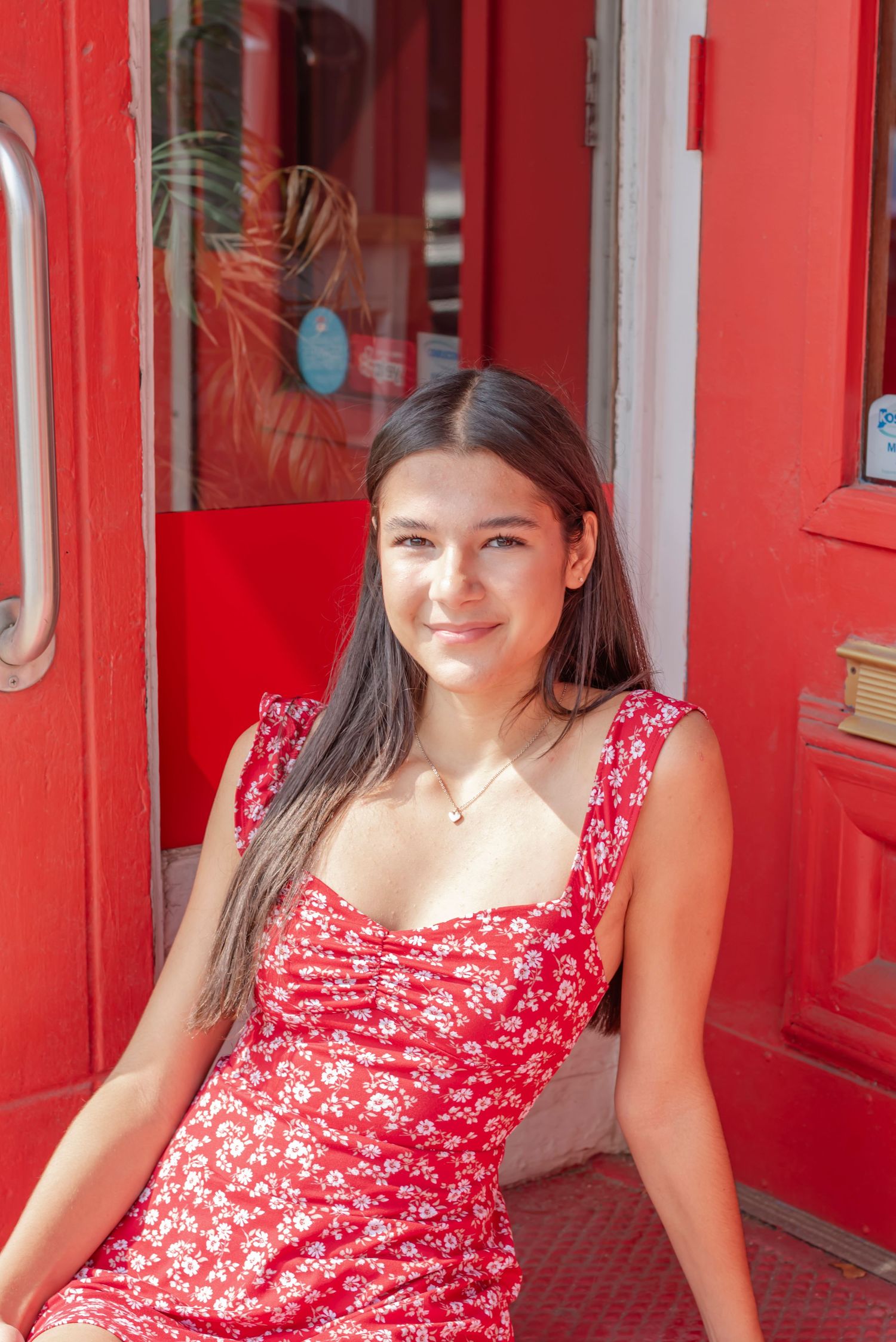 A bright red doorway frames a summery scene with a floral dress and natural lighting.