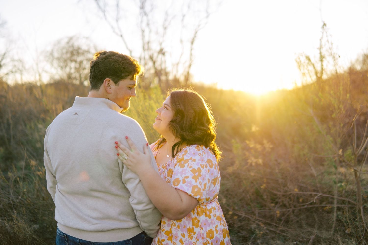 A romantic couple shares a tender moment at golden hour in a field backlit by the setting sun.