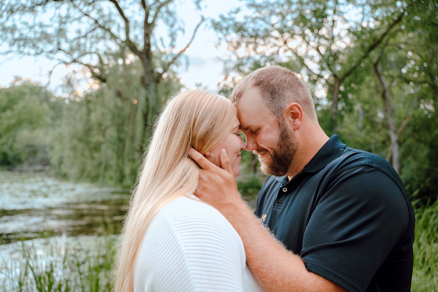 Intimate couple's portrait by a lake with overhanging trees in natural lighting.