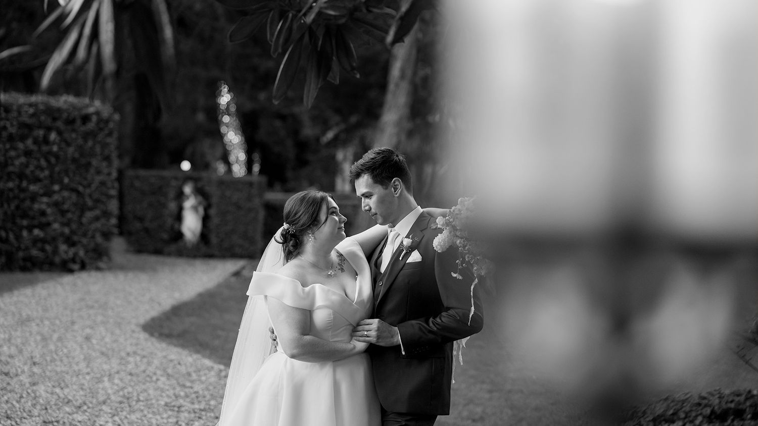 A black and white wedding photograph showing a tender moment between newlyweds in an outdoor garden setting at Gabbinbar in Toowoomba