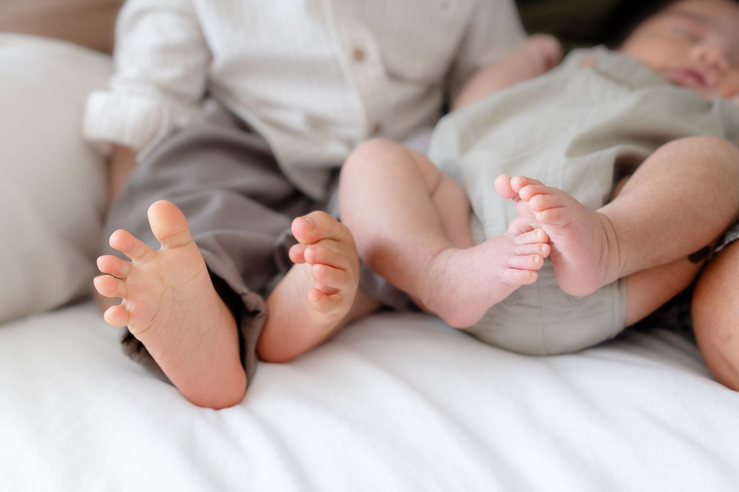 Close up view of tiny baby feet on white bedding showing siblings resting together.