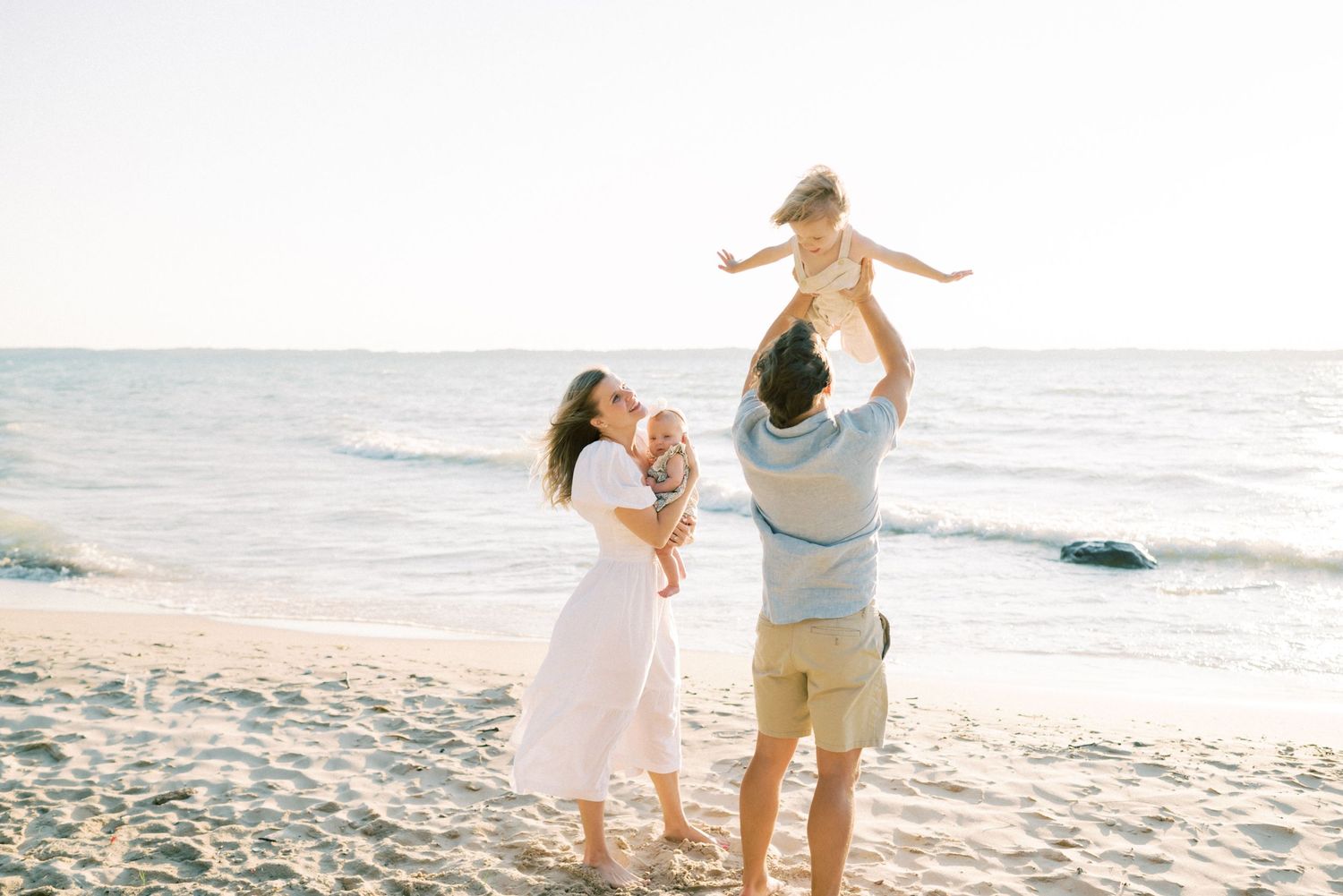 A family shares a joyful moment playing together on a sunny beach at sunset.