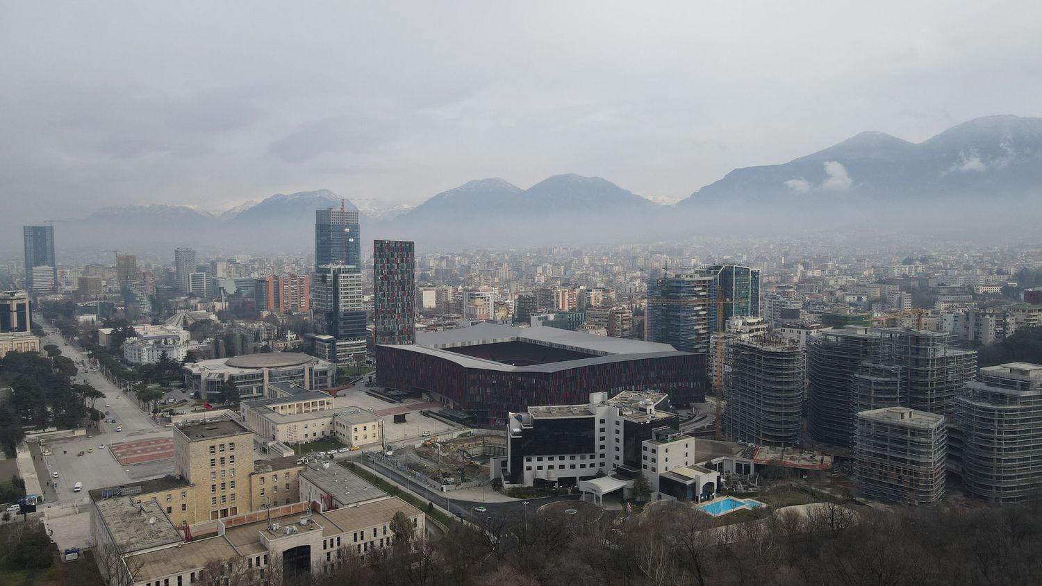 Cityscape view of Tirana with mountains in the background and modern buildings in the foreground.