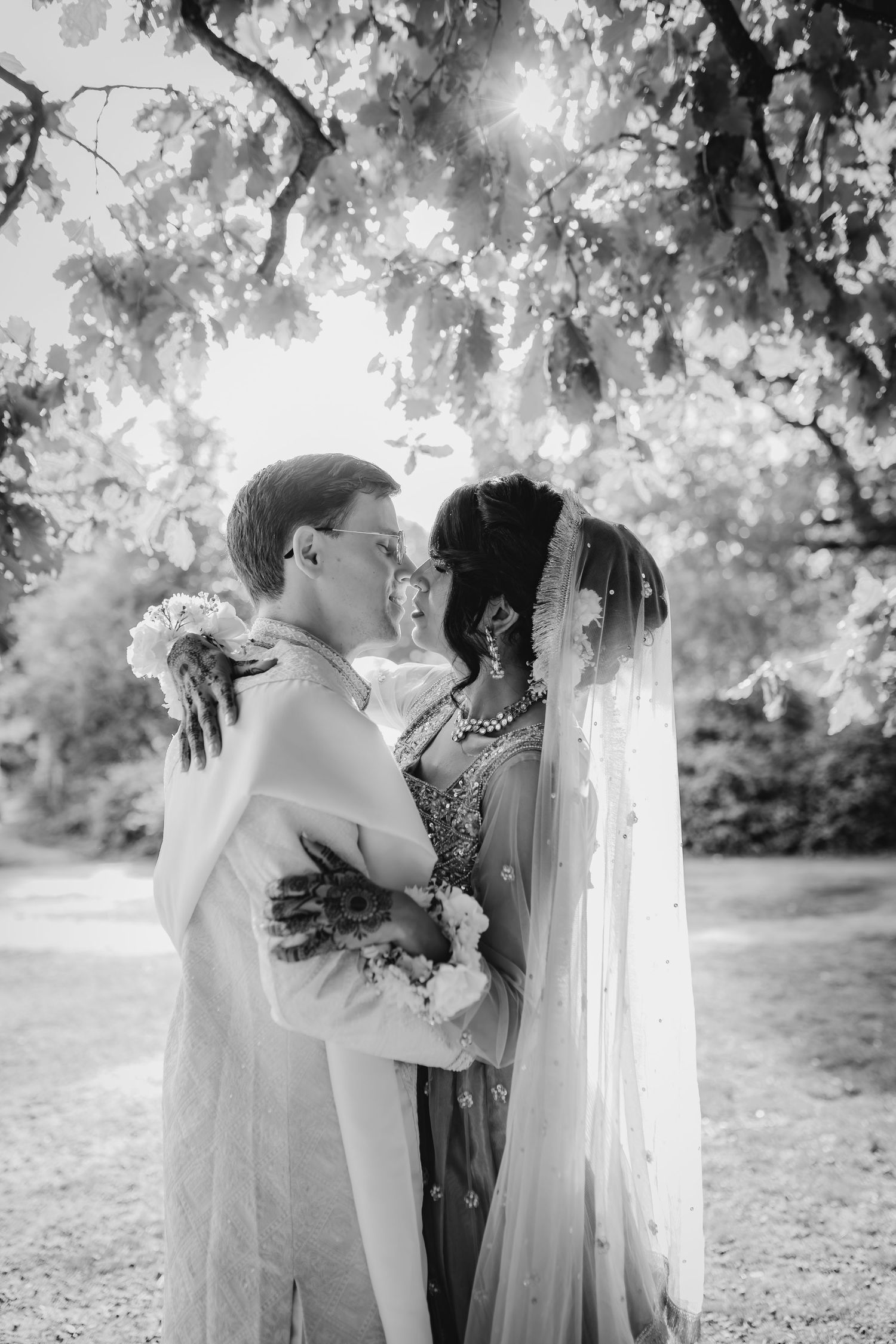 A black and white romantic photo sequence showing two people embracing under sunlit trees in a garden setting.