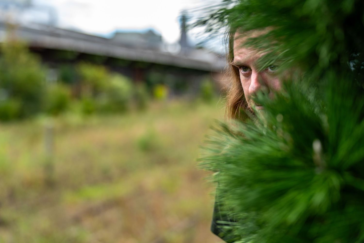 Person wearing black cropped sweater and jeans poses in front of lush green foliage in outdoor portrait series.