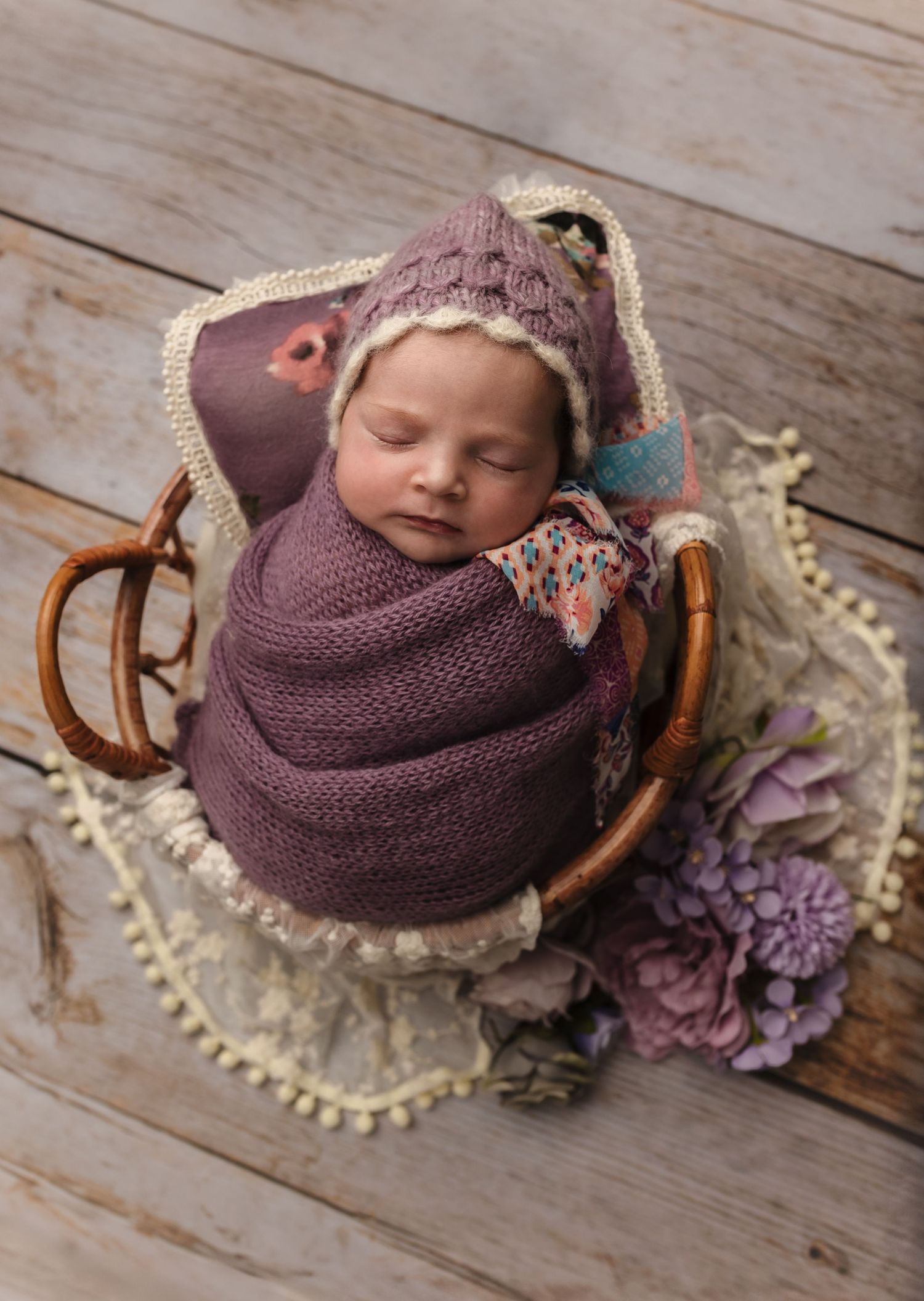 Newborn girl sleeping peacefully in a boho-style basket, wrapped in soft purple swaddle during a studio newborn session in Charlottesville,