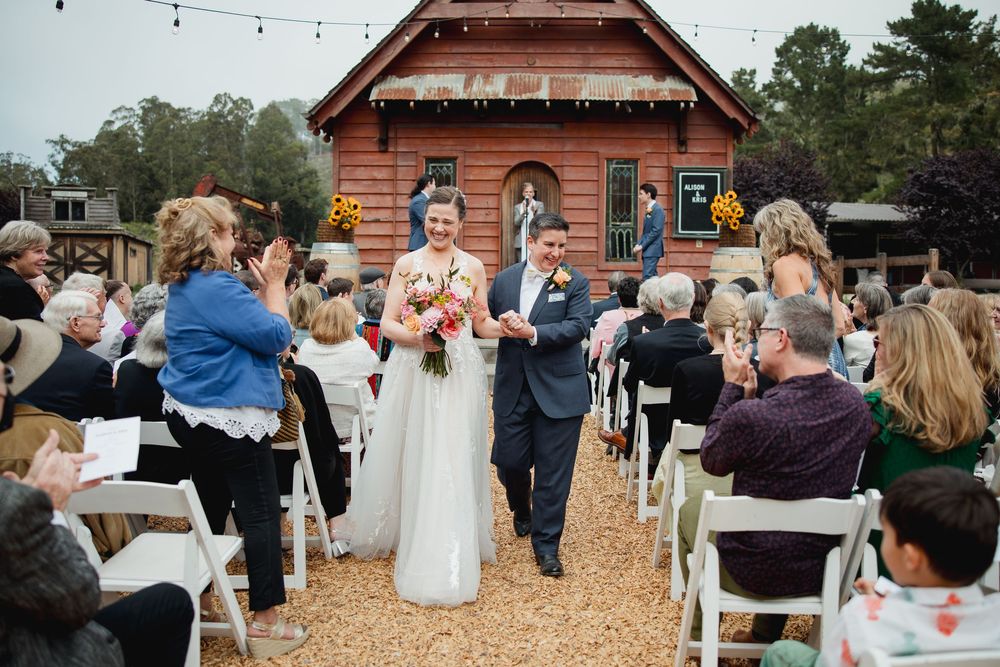 Outdoor wedding ceremony with string lights and rustic barn setting during golden hour.