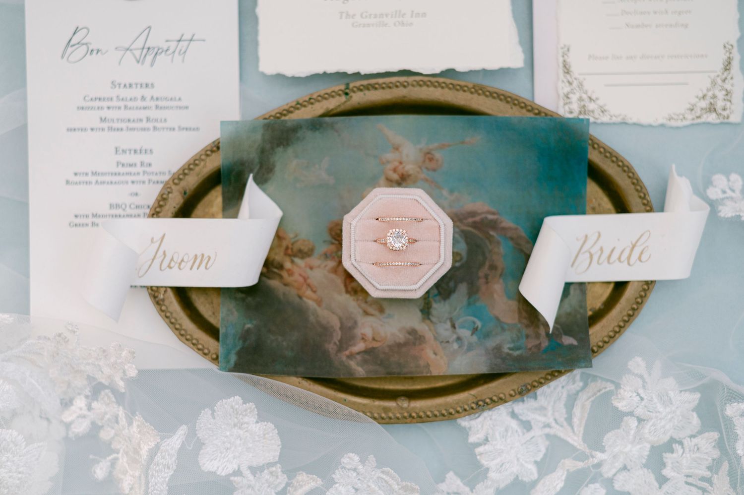 Elegant wedding invitation suite in white and gold with floral details laid out on a light blue surface.