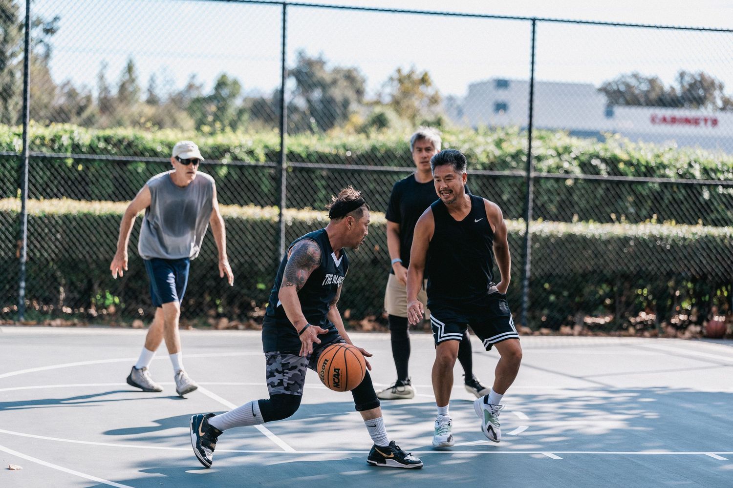 Basketball players practice defensive drills and agility exercises on an outdoor court during a training session.